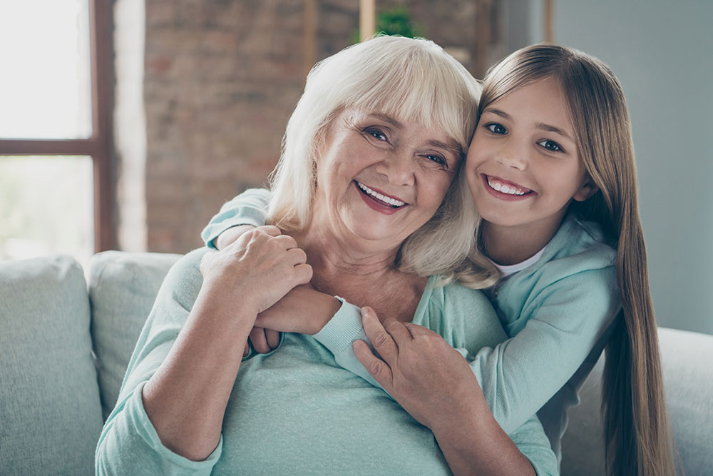 Close up photo of two best friends people cute aged grandma small grandchild girl sitting comfortable sofa hugging piggyback spending weekend together house indoors